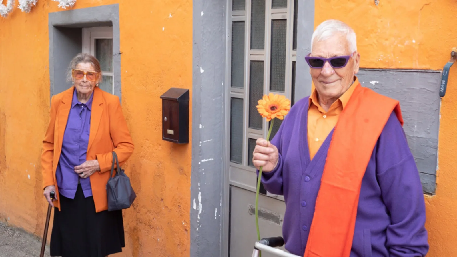 Elderly couple with a cane and a walker on a street of colorful houses