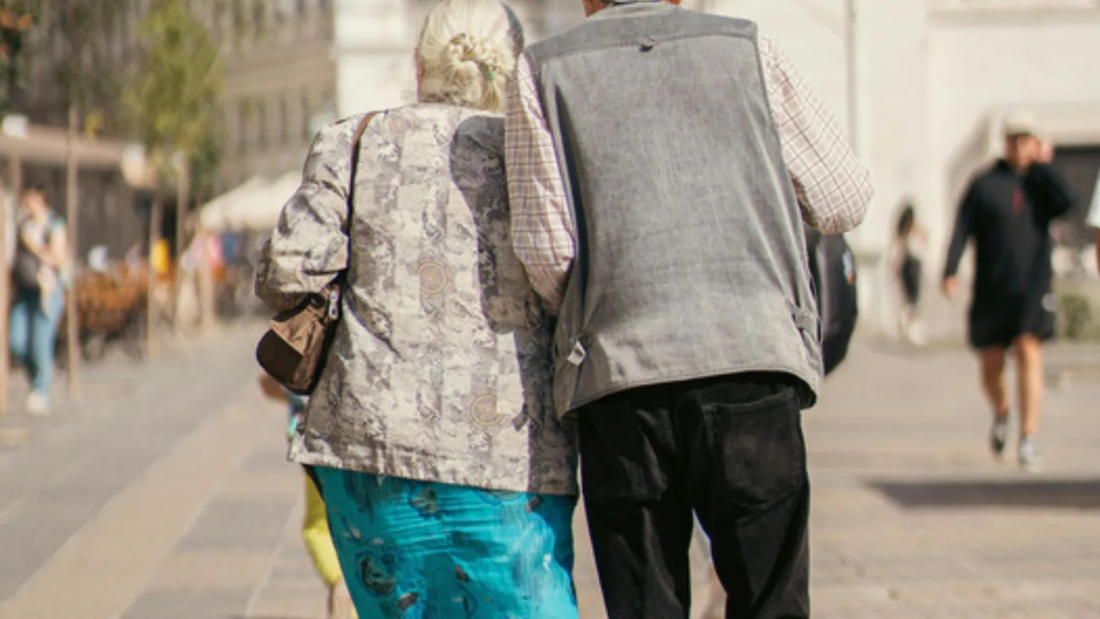 Elderly couple walking arm in arm along a paved city street