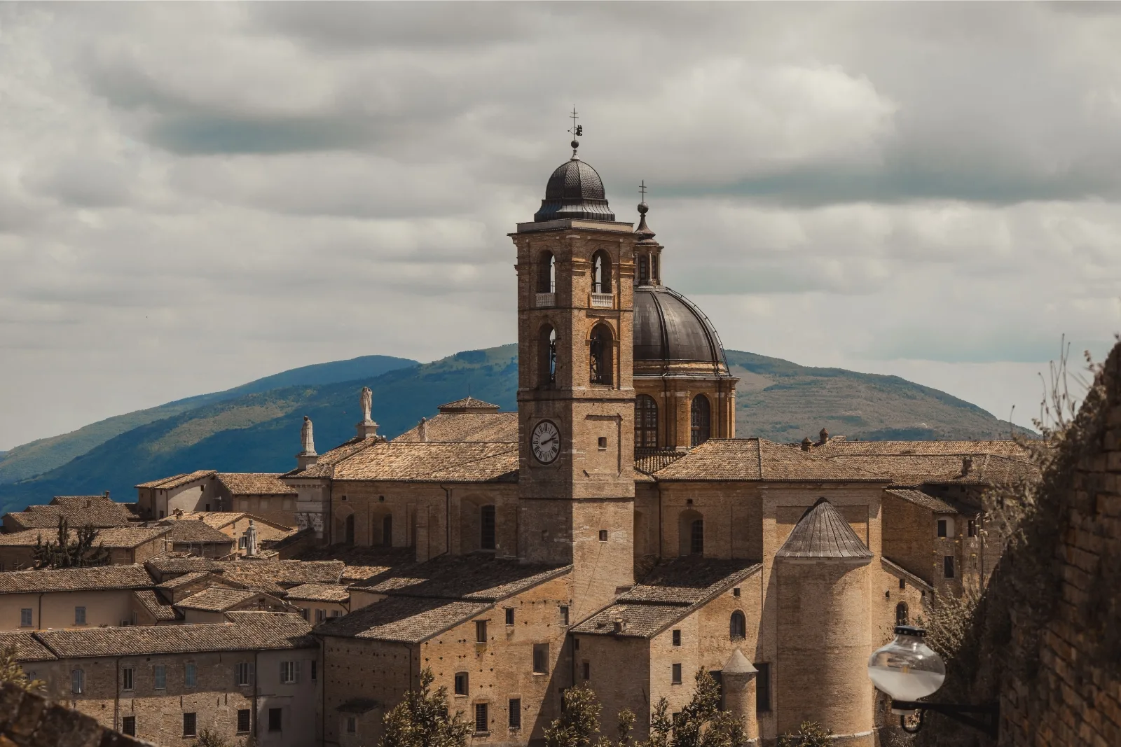 The bell tower and dome of Urbino Cathedral above the rooftops of the old town, with hills behind